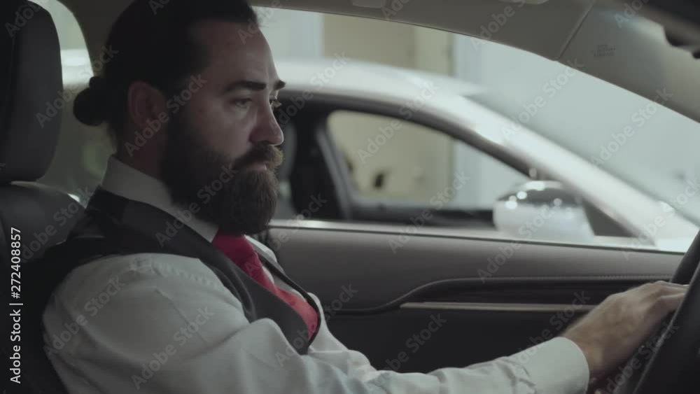 Portrait attractive successful bearded businessman sitting in the vehicle and inspects newly purchased auto from the car dealership. Car showroom. Advertising concept.