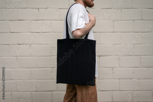 Urban mockup of tote bag. Men holding black cotton tote bag on a brick wall background. Template can be used for you design 