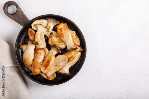 Fried eryngii mushrooms in cast-iron pan on white table. Grilled slices of king oyster mushrooms. Top view, copy space. photo