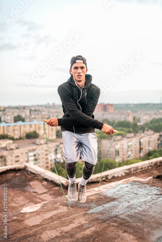 exercising and lifestyle concept - man skipping with jump rope outdoors on the roof