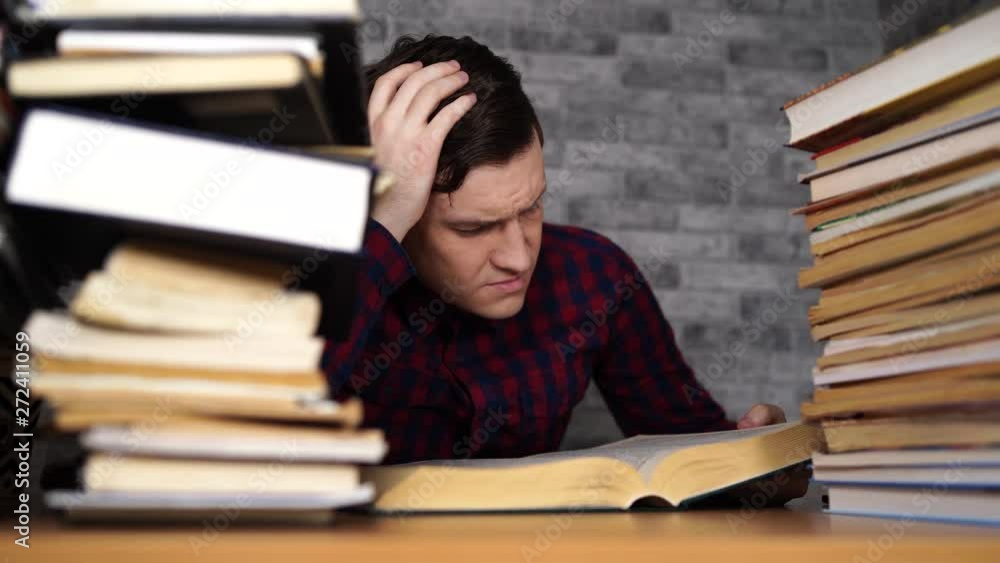 Man student boring reading book at library with a lot of books in university. Student disheartened reading book for examination. Man student boring reading book at library with a lot of books in university. Student disheartened reading book for examination.