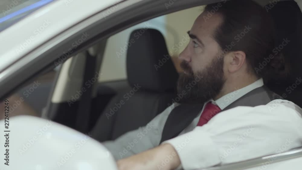 Portrait attractive confident bearded businessman sitting in the vehicle and inspects newly purchased auto from the car dealership. Car showroom. Advertising concept. Portrait attractive confident bearded businessman sitting in the vehicle and inspects newly purchased auto from the car dealership. Car showroom. Advertising concept.