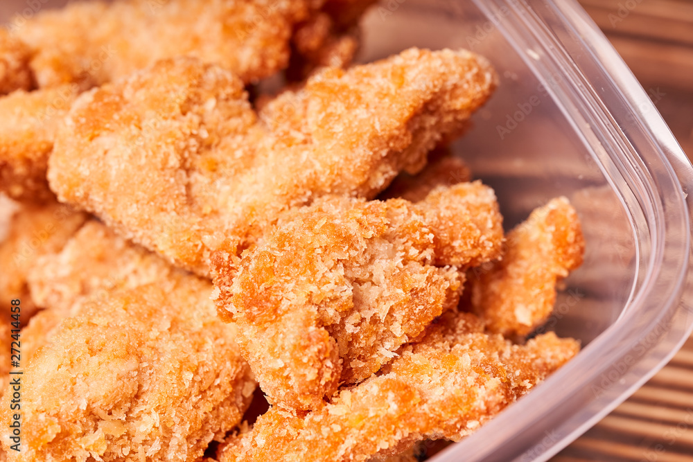 Chicken strips in a plastic container on a wooden table. Chicken strips in a plastic container on a wooden table.