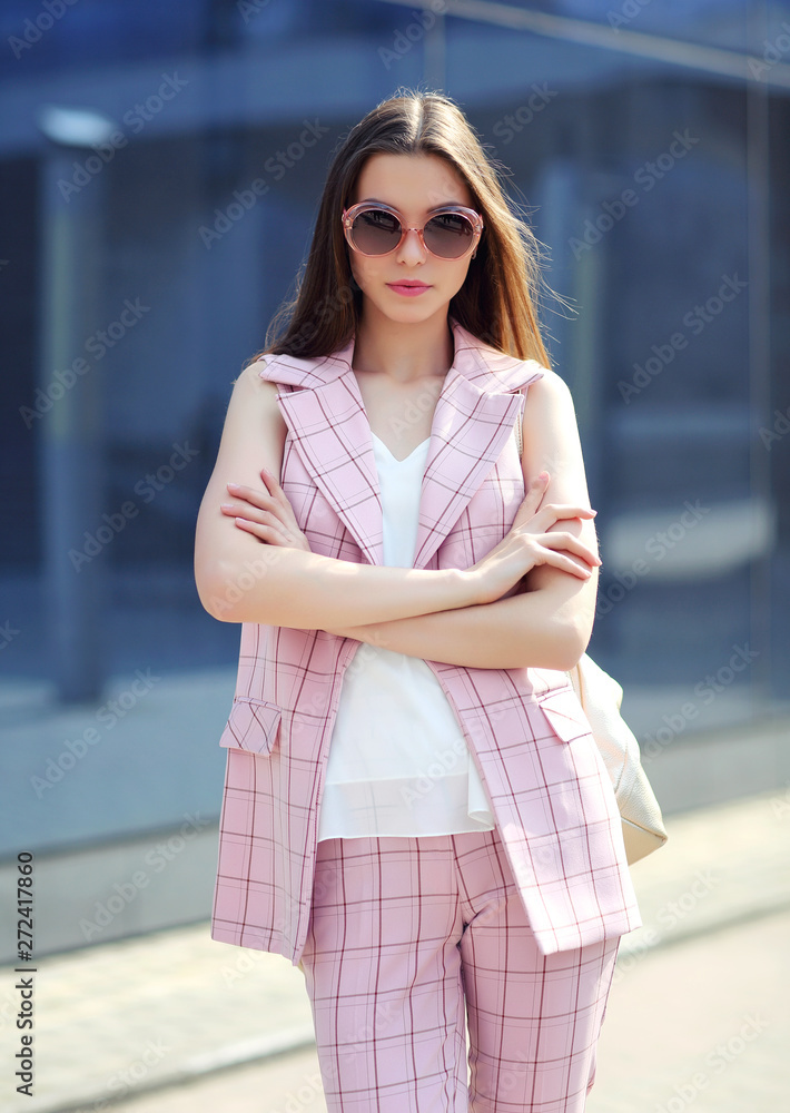 high fashion outdoor Portrait of a young woman. Pantsuit, pink color, long hair, sunglasses