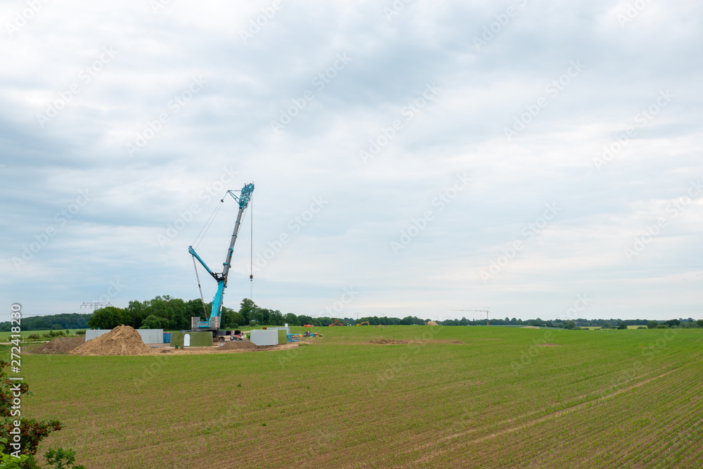 in the middle of a field, a wind turbine is erected with the help of a large crane