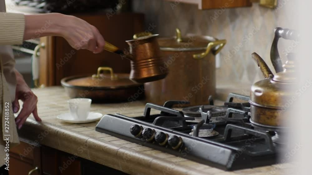 Close up of Caucasian blonde businesswoman standing at stove, taking jezve and pouring coffee into white cup and then drinking it Close up of Caucasian blonde businesswoman standing at stove, taking jezve and pouring coffee into white cup and then drinking it