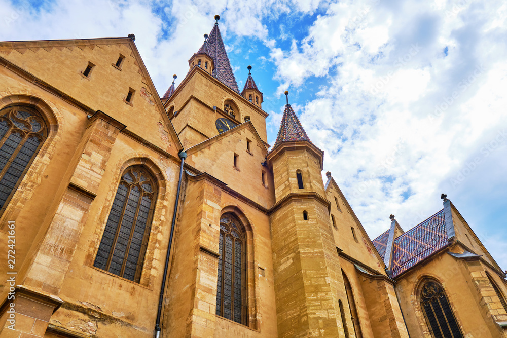 Gothic-style Lutheran Cathedral of Saint Mary (Catedrala Evanghelica C.A. Sfanta Maria / Evangelische Stadtpfarrkirche) in Sibiu, Romania - low angle with beautiful white clouds and blue sky.
