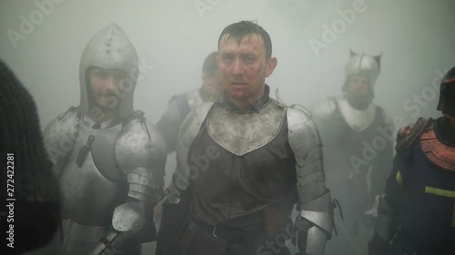 Combat squad of medieval knights of the Crusaders stand in armors and helmets with their swords and shields preparing to attack  against background of smoke in the forest.