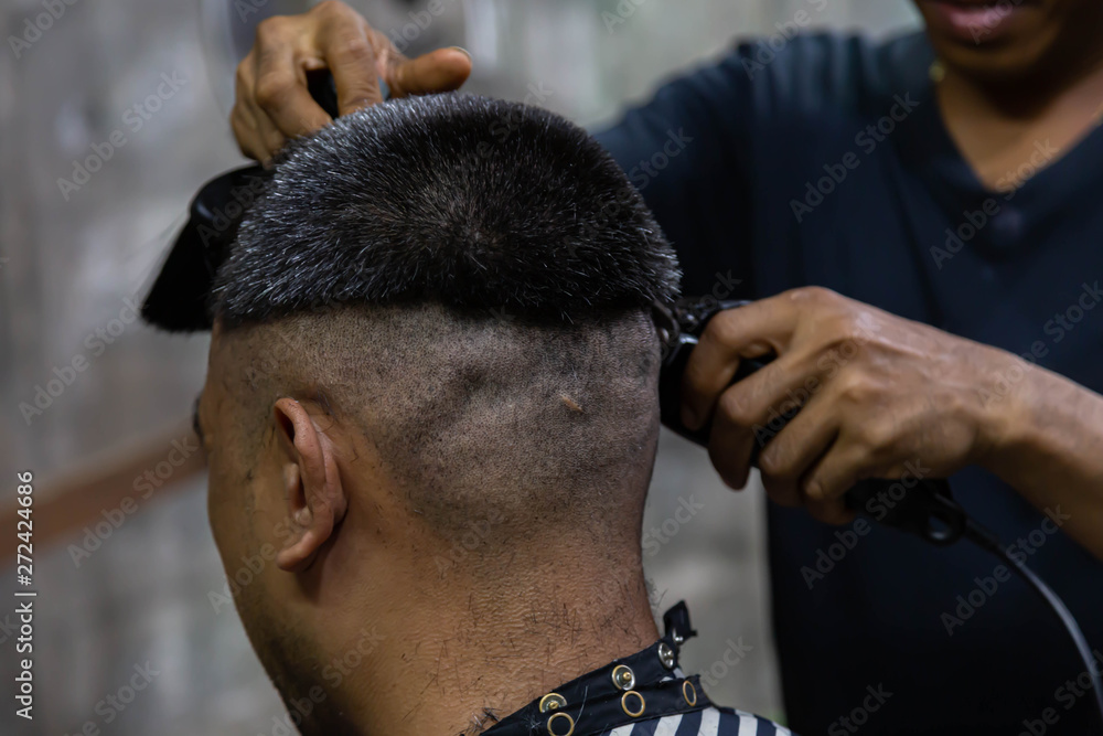 Fototapeta premium A male hairdresser that provides customer service, makes hair cut using a machine and comb.
