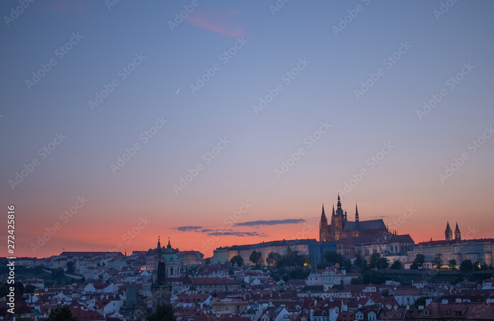 Orange sky sunset behind Prague Castle, with crescent moon in sky