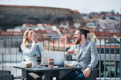 Bilde på lerret Two young business people sitting on a terrace outside office, having lunch break