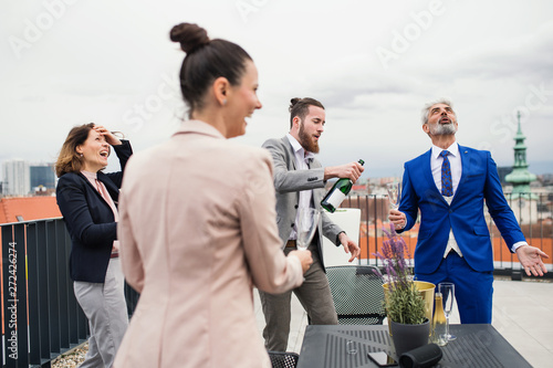 A group of joyful businesspeople having a party outdoors on roof terrace in city.