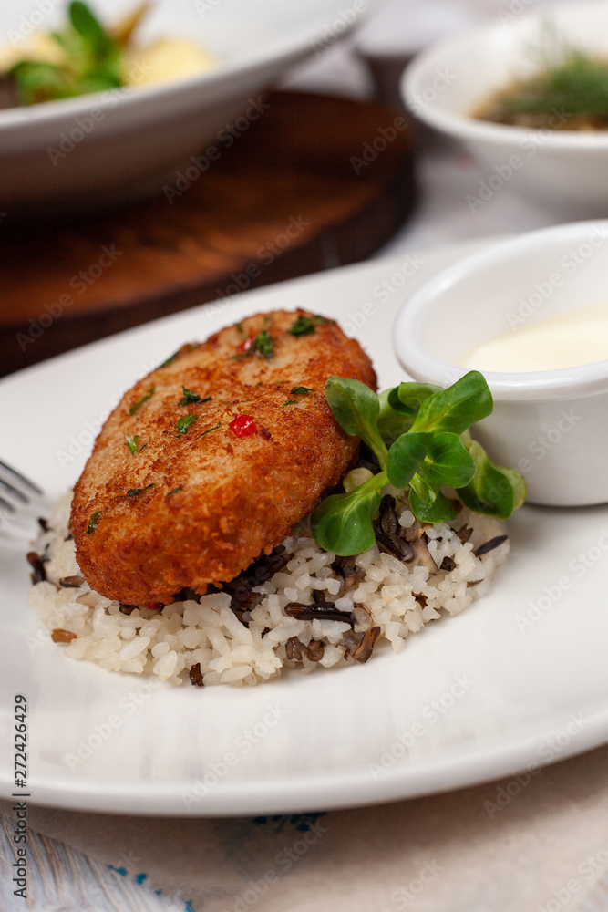 Close up of crunchy breaded cutlet with white steamed basmati rice and mayo as a part of restaurant set menu, served in a white plate