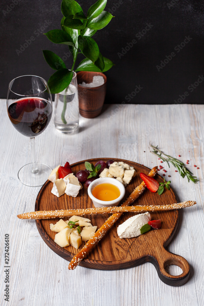 Assorted cheese for wine: bread sticks, bree, gouda, honey, parmesan, camembert and strawberries, served on a wooden board, on a black and white background