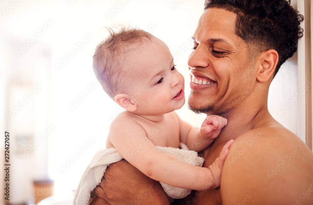 Father and small toddler son wrapped in towel in a bathroom indoors at home. Father and small toddler son wrapped in towel in a bathroom indoors at home.