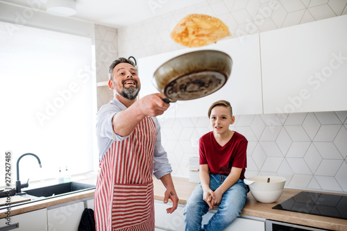Fotografi Mature father with small son indoors in kitchen, flipping pancakes