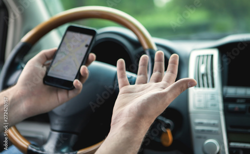 a young man at the wheel uses the phone as a navigator
