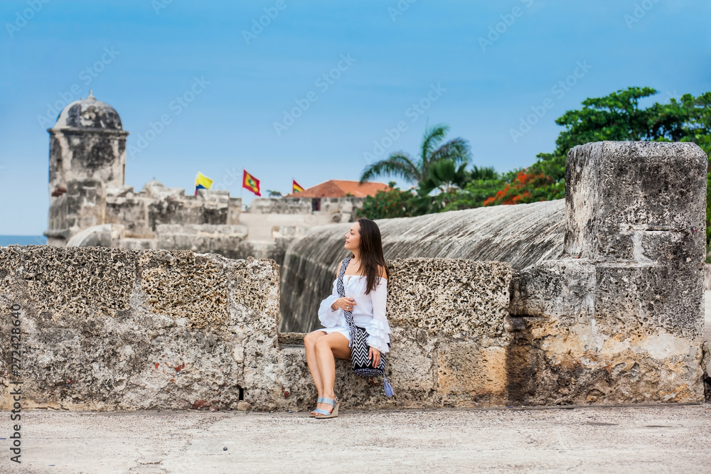 Beautiful woman on white dress sitting alone at the walls surrounding the colonial city of Cartagena de Indias