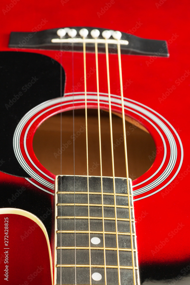 Closeup of a six stringed red acoustic guitar, from fingerboard side. Music entertainment background.