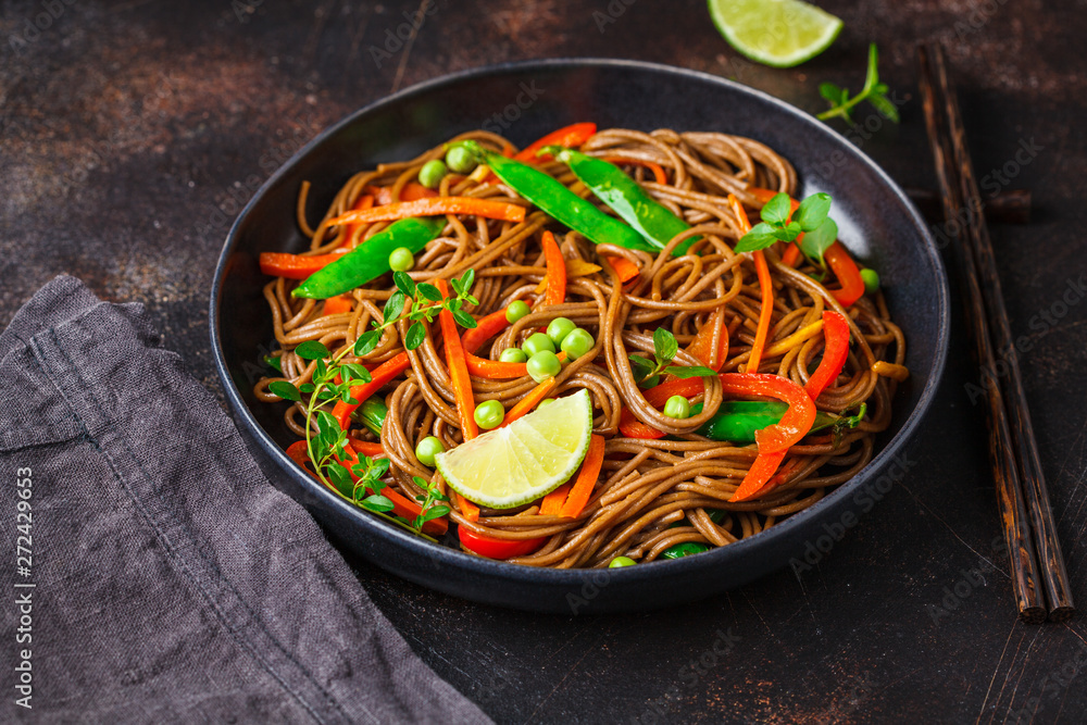 Vegan buckwheat soba noodles with vegetables in black plate on dark background. Vegan buckwheat soba noodles with vegetables in black plate on dark background.