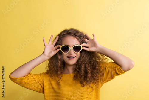 Portrait of a young woman with sunglasses in a studio on a yellow background.