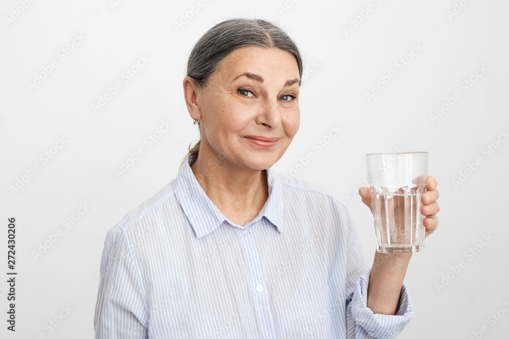 Picture of positive energetic middle aged woman with wrinkled face, enjoying warm fresh drinking water in the mornings which is good for digestion. Wellness, age, dietary habits and health concept