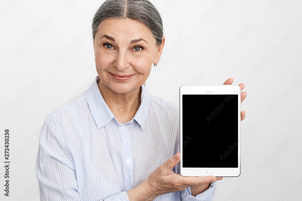 People, age and modern technology concept. Portrait of successful mature gray haired businesswoman in blue shirt holding generic digital tablet with blank copyspace display for your information People, age and modern technology concept. Portrait of successful mature gray haired businesswoman in blue shirt holding generic digital tablet with blank copyspace display for your information