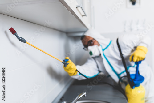 Exterminator in work wear spraying pesticide with sprayer. Selective focus.