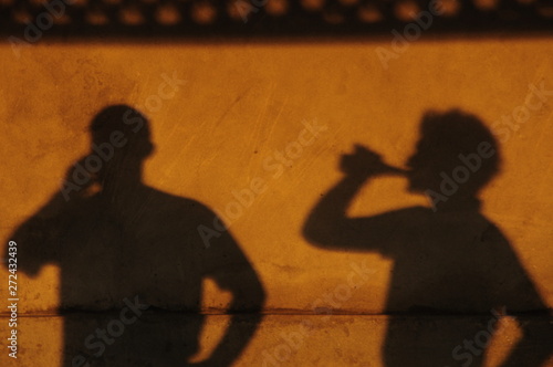 Shadow of people drinking on a yellow wall.