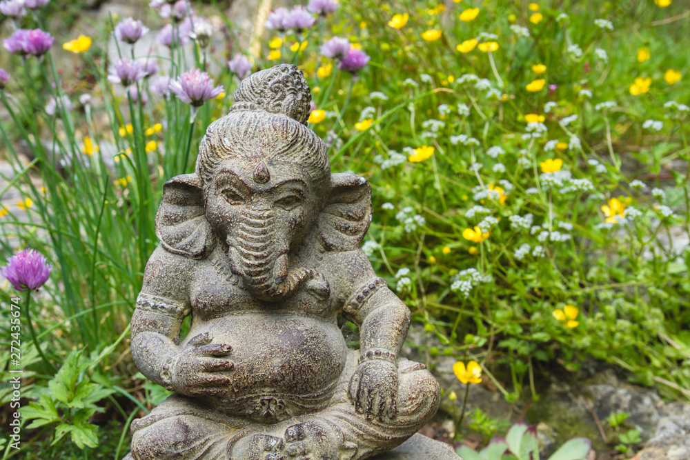 Ganesh stone statue in a springtime garden with flowers Ganesh stone statue in a springtime garden with flowers