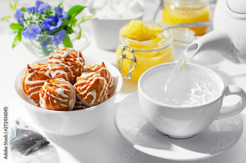 Cup of hot tea with cookies and honey on a white background. The process of pouring boiling water, tea bags. Flowers in the background, selective focus.