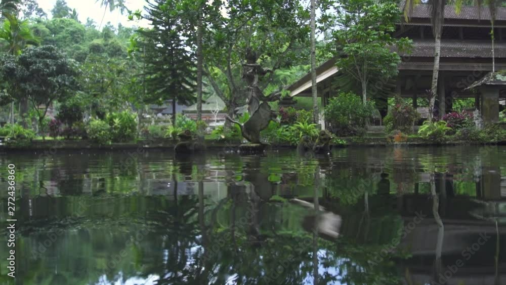 Indonesia god statue in decorative fish pond on green garden landscape. Ancient traditional architecture in Bali, Indonesia. Asian culture. Travel concept. Indonesia god statue in decorative fish pond on green garden landscape. Ancient traditional architecture in Bali, Indonesia. Asian culture. Travel concept.