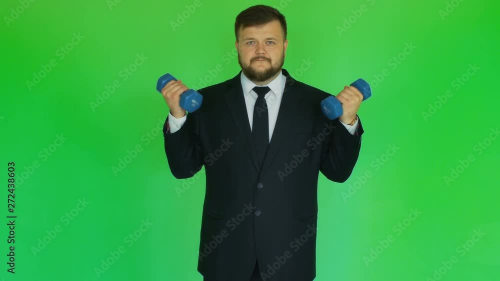 Concept of businessman and health. Man in suit doing exercises with dumbbells on chromakey green. Plump bearded person in jacket, shirt, tie and trousers does exercises in the sport gym. Green Concept of businessman and health. Man in suit doing exercises with dumbbells on chromakey green. Plump bearded person in jacket, shirt, tie and trousers does exercises in the sport gym. Green