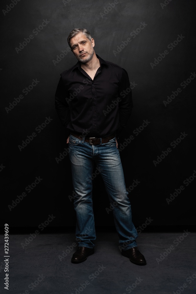 Full body portrait of middle-aged good looking man posing in front of a black background with copy space.
