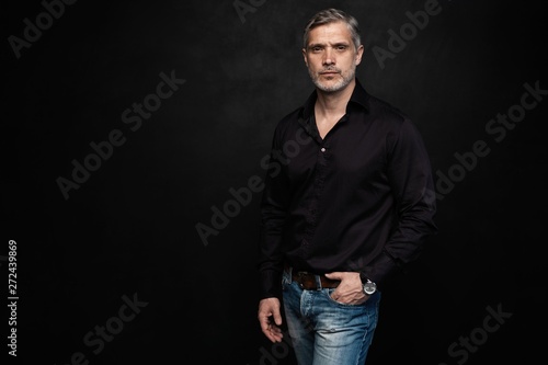 Middle-aged good looking man posing in front of a black background with copy space. © opolja