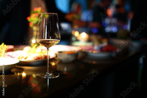 A glass of wine on a table with a blurred snack in the background in warm light