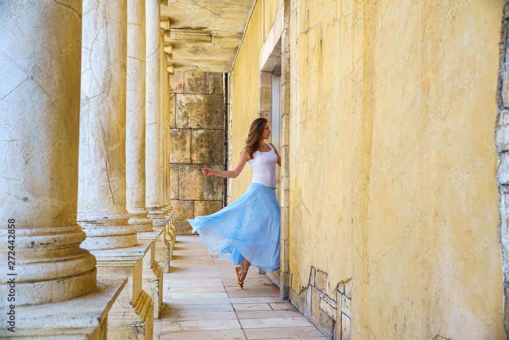 Girl runs away in dance in the door in blue airy skirt in ancient ruins walls and columns in Macao Girl runs away in dance in the door in blue airy skirt in ancient ruins walls and columns in Macao