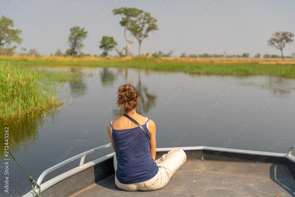 eine junge Frau sitzt auf einem Ausflugsboot, das durch das Okavango Delta fährt