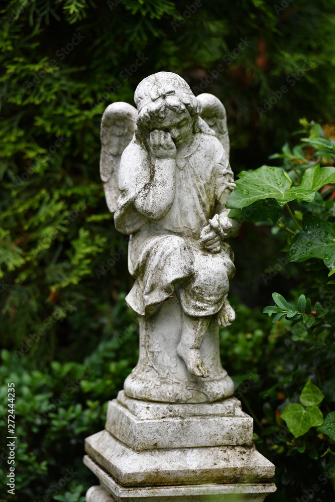 A white, weathered statue of a sad angel on a christian cemetery in Berlin-Germany.