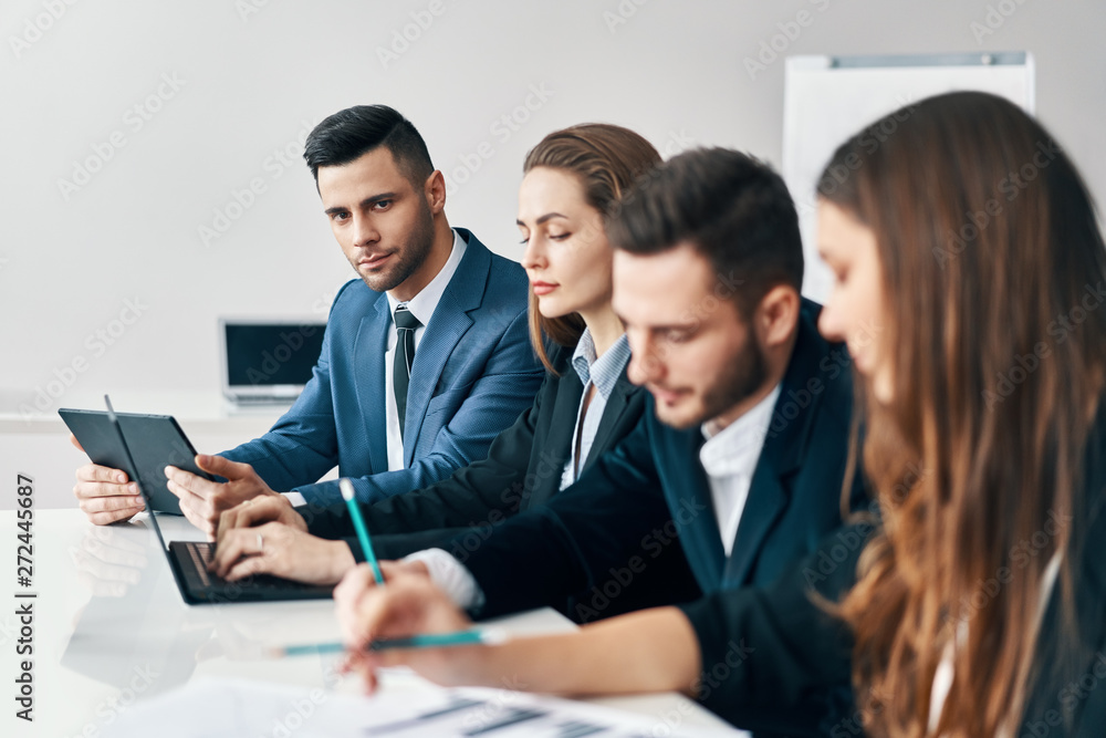 Portrait of smiling group of business people sitting in a row together at table in a modern office Portrait of smiling group of business people sitting in a row together at table in a modern office