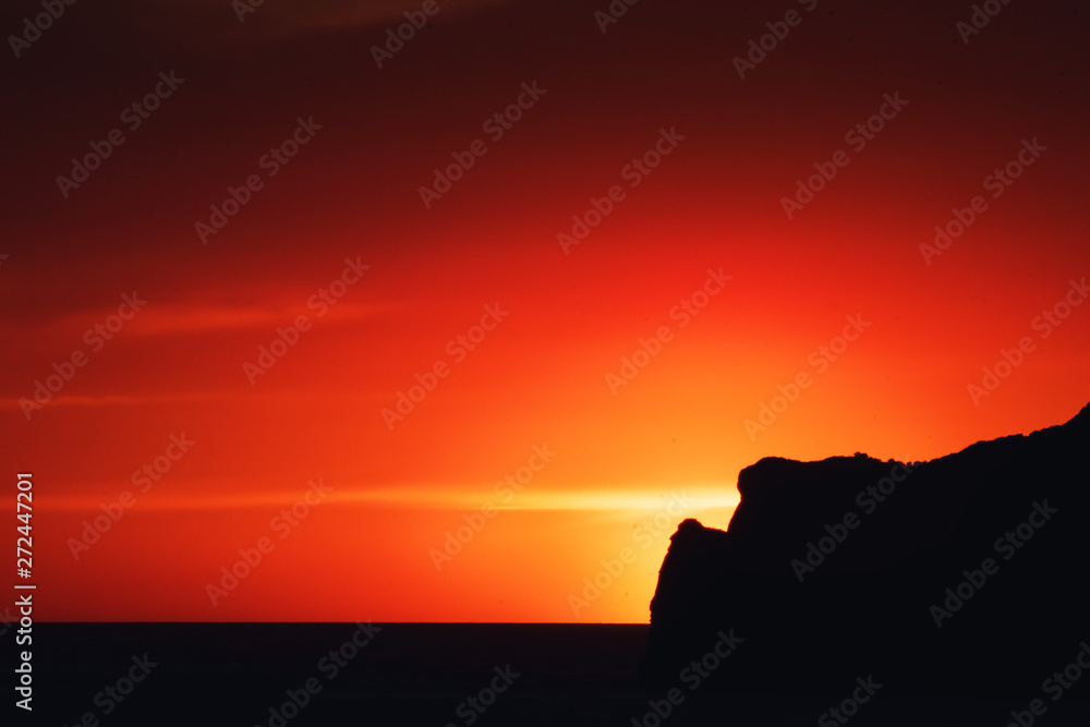 Dramatic ocean sunset scene with giant big sun setting behind a rock coastline silhouette an colorful sky glow. Port Andratx, Mallorca, Spain Dramatic ocean sunset scene with giant big sun setting behind a rock coastline silhouette an colorful sky glow. Port Andratx, Mallorca, Spain