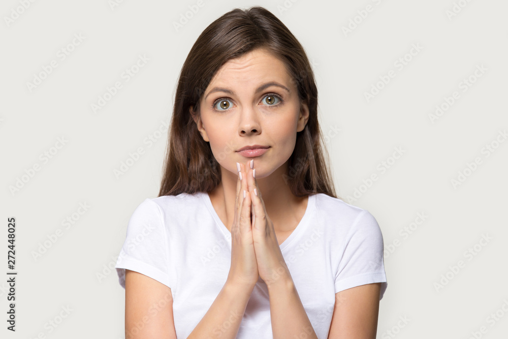 Millennial woman holds hands together praying pose over gray background Millennial woman holds hands together praying pose over gray background