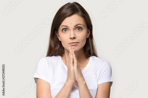 Millennial woman holds hands together praying pose over gray background