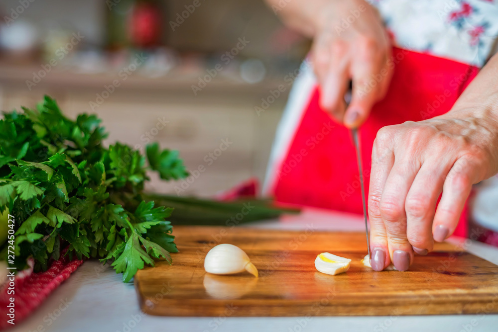 Female hand with knife chops garlic in kitchen. Cooking vegetables