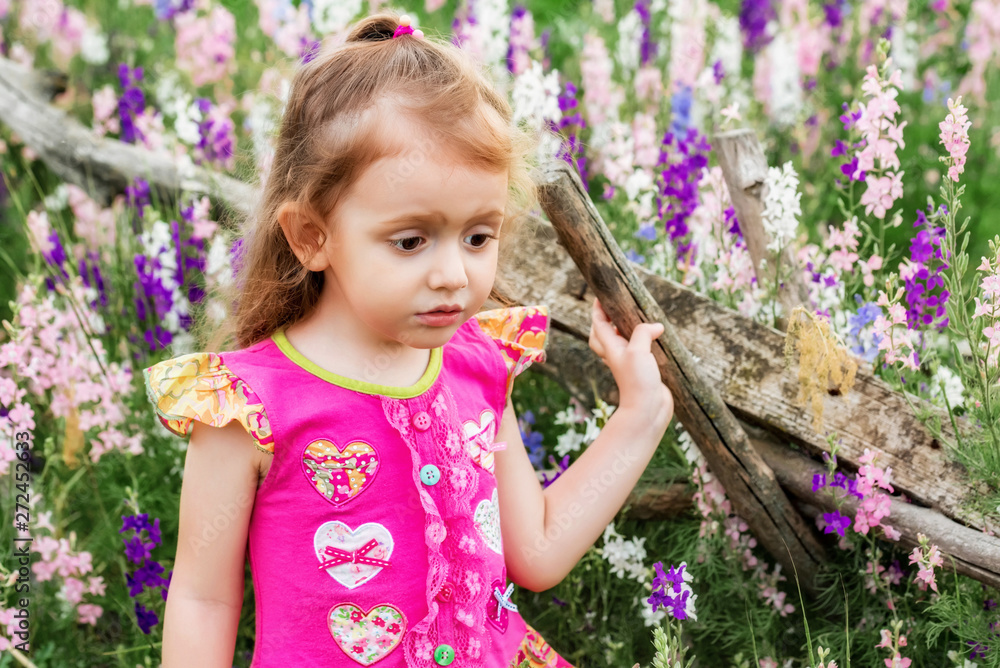 Cute sad baby girl in bright dress looks down outdoors in green field Cute sad baby girl in bright dress looks down outdoors in green field