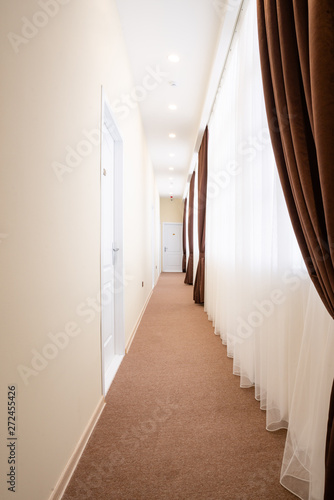 Bright corridor with white doors, brown carpet, white tulle curtains and brown curtains.