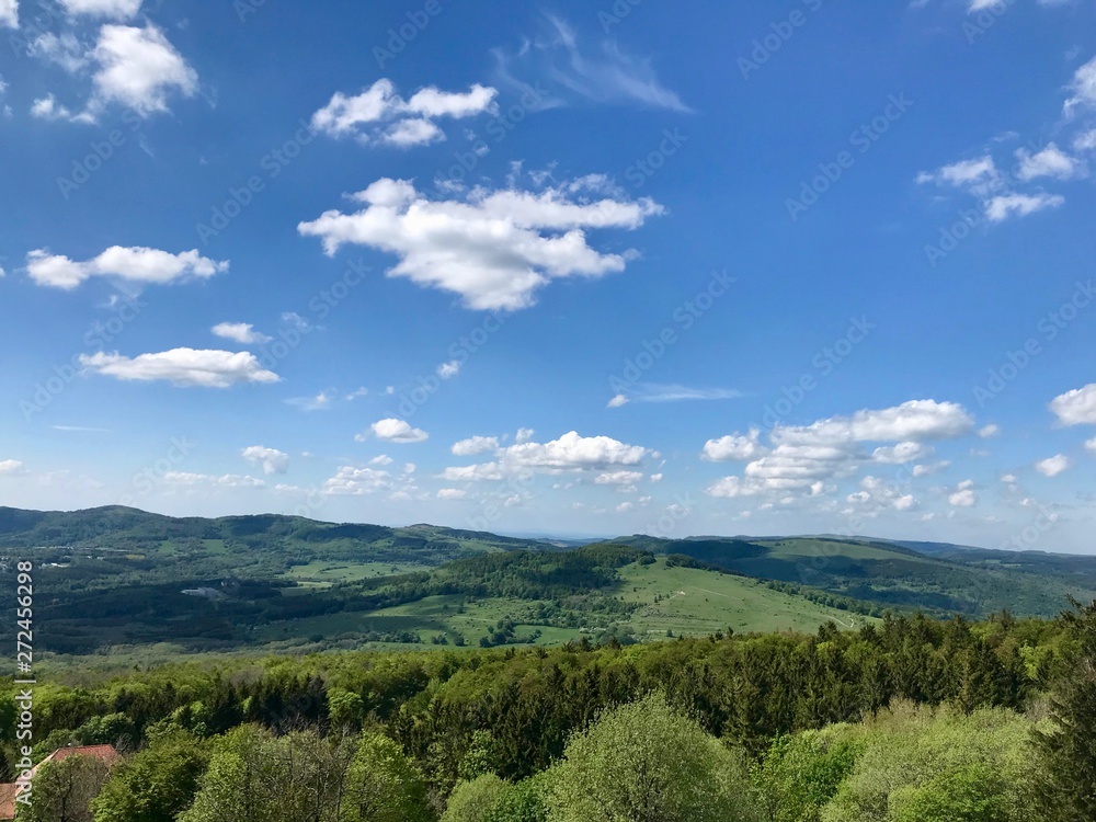 Scenic hike to the Kreuzberg (Calvary) in the Bavarian Rhoen region (Germany) on a beautiful sunny summer day through lush green landscape with grass, trees and a blue sky with white clouds