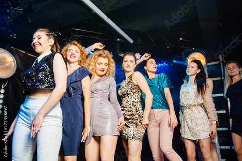 A group of young women dancing at nightclub. Joyful emotional girls relaxing and raising her hands during dance with friends standing in a row during music festival in nightclub.