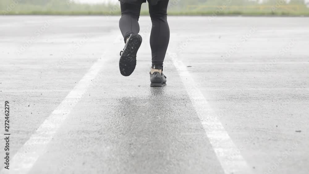 Slow motion shot of legs of a runner in sneakers. Male sports man jogging outdoors. Single runner running in rainy weather. Close up. Slow motion shot of legs of a runner in sneakers. Male sports man jogging outdoors. Single runner running in rainy weather. Close up.