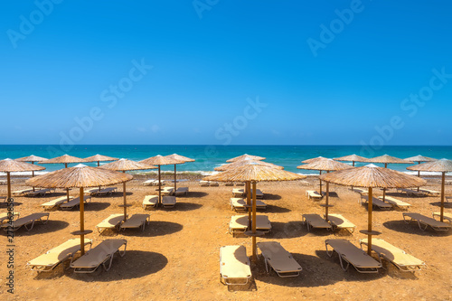 Sun loungers with parasols on the sea beach. Beach recreation view. Sand shore. Sunbathing on the beach. Seaside. Relax. Leisure.